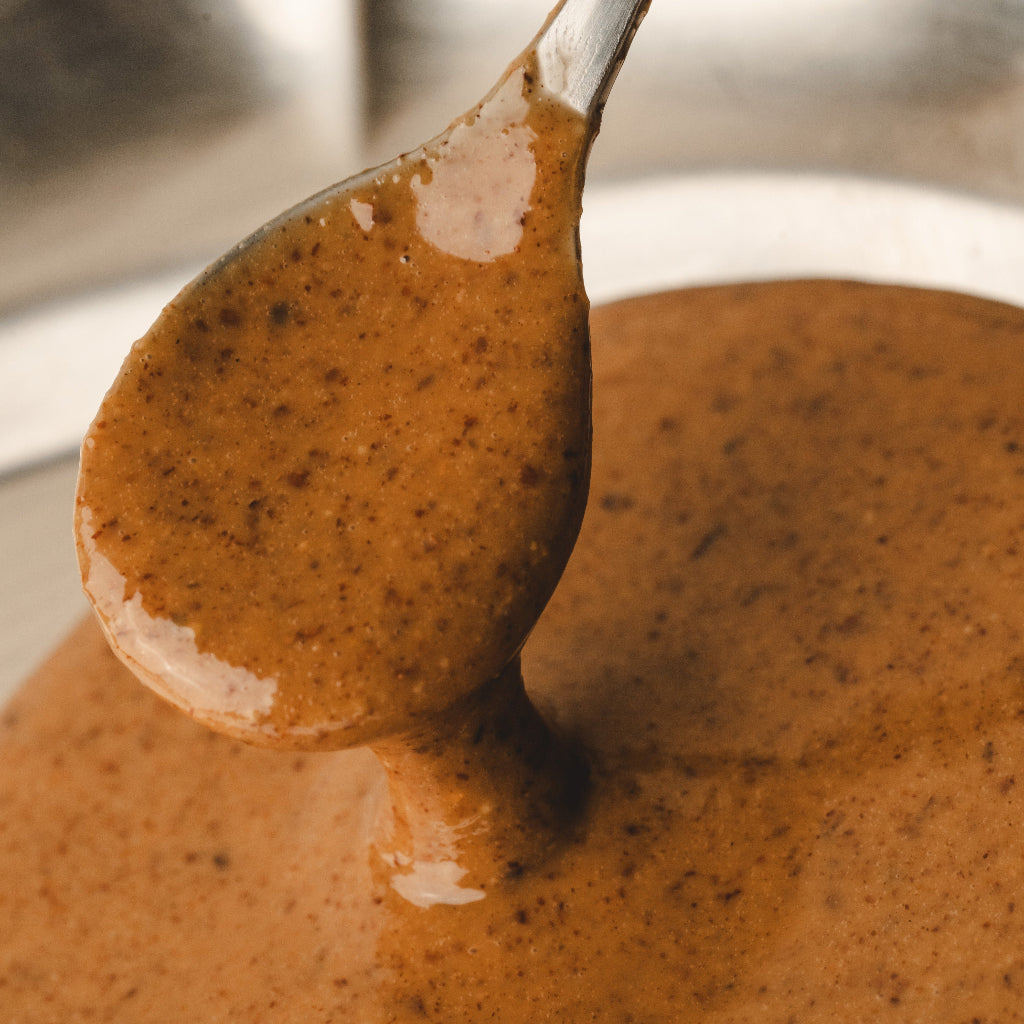 Spoon with creamy brown sauce over a blurred background